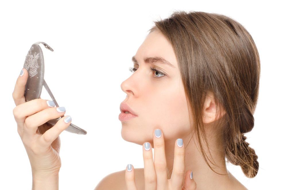 Woman examining her face in a handheld mirror