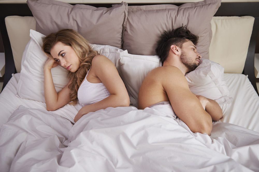 Couple in bed with their backs to each other frustrated from erectile dysfunction