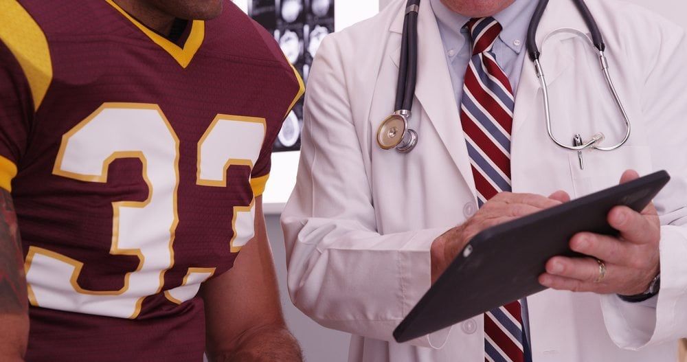 Doctor with a notepad talking with football player