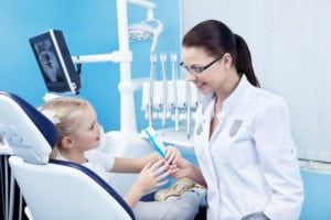 Child sitting in dental chair speaking to her dentist